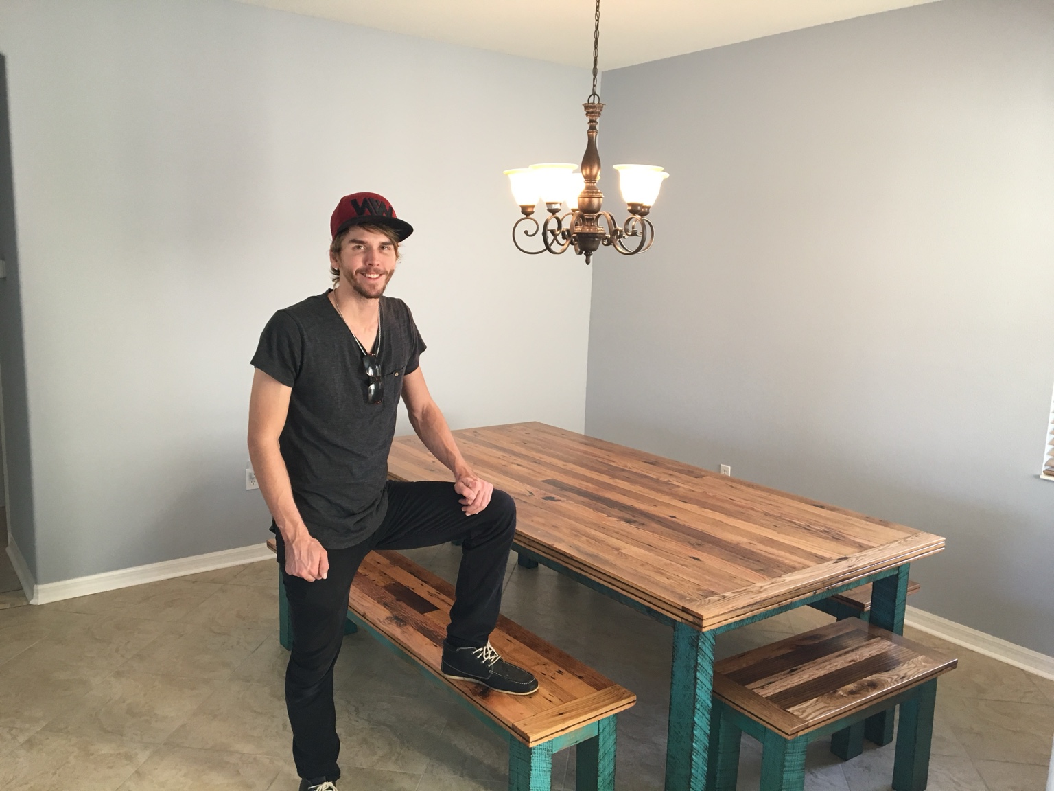 Dining table with matching benches and turquoise painted bases, shown with a person beside it